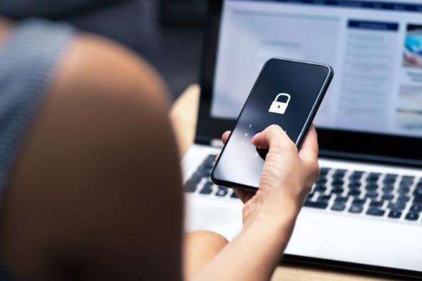 Women holding a locked phone in front of an laptop